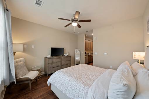 Guest suite bedroom at The Dorset with dresser, TV, seating chair, and view toward kitchenette area