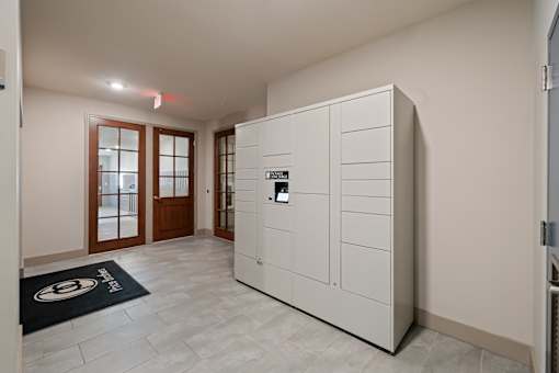A white cabinet with a black handle is in a room with a black mat on the floor.
