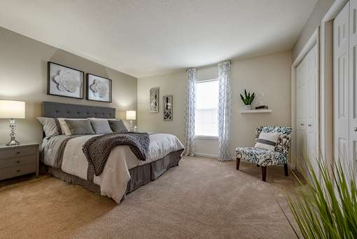 A bedroom with a bed, chair, and two framed pictures on the wall.