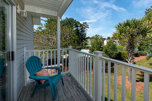 A blue chair sits on a porch with a view of a yard and trees.