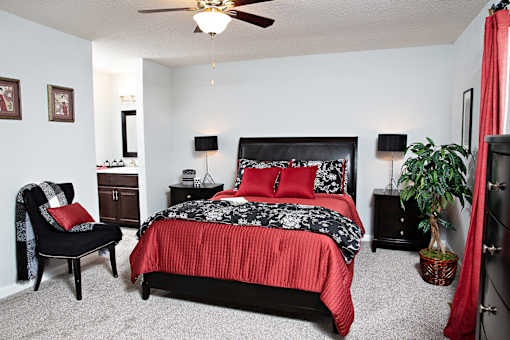 A bedroom with a red bedspread and a black chair.