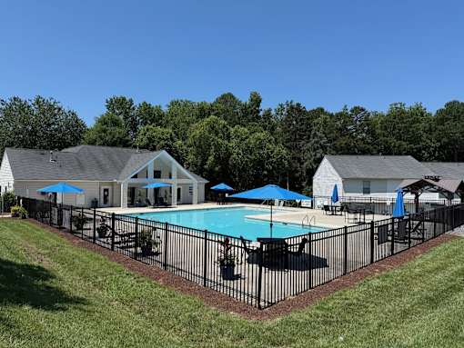 A pool surrounded by a black fence with a house in the background.
