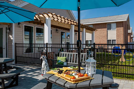 A picnic setup on a patio with a blue umbrella and a tray of food.