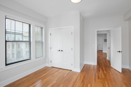 a living room with white walls and wood floors and a door to a hallway