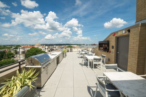 a rooftop patio with tables and chairs and a barbecue grill
