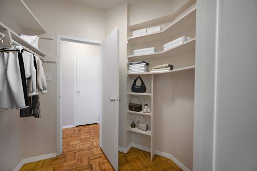 A hallway with a white door and a white closet with a shelf and a black speaker.