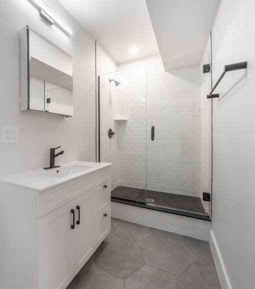 A white bathroom with a sink, mirror, and walk-in shower.