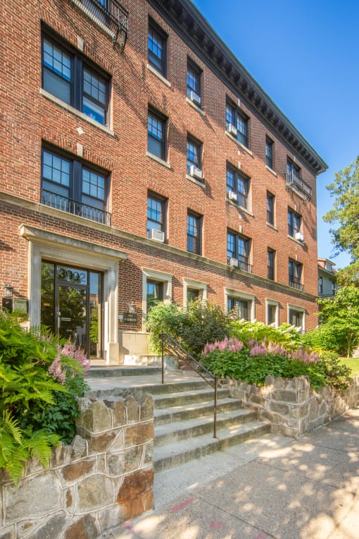 the front of a brick building with stairs and plants