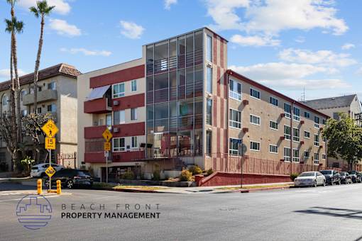 A multi-story building with a red and beige facade is under construction with a sign that reads "BEACH FRONT PROPERTY MANAGEMENT".