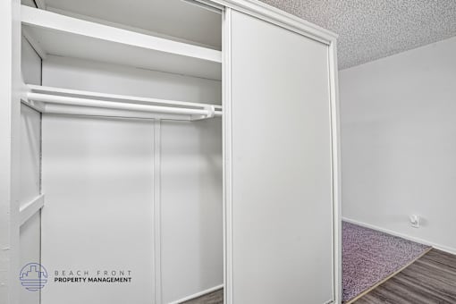 A white closet with a shelf and a purple rug on the floor.