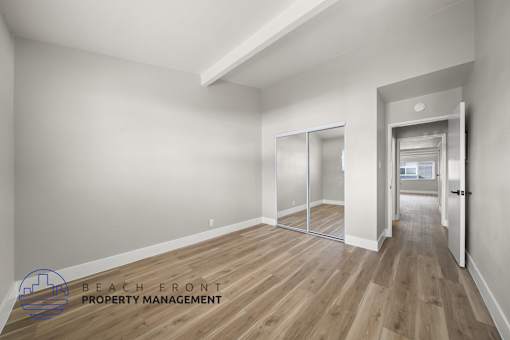 A spacious room with wooden flooring and a logo for Beach Front Property Management in the corner.