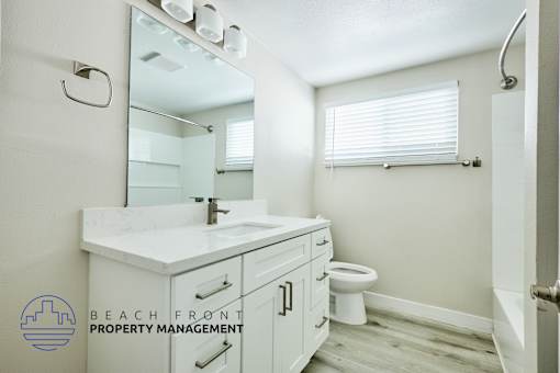 A bathroom with a sink, mirror, toilet and a window with blinds.