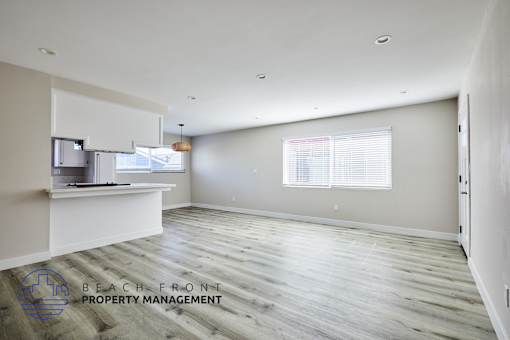 A spacious room with wooden flooring and a window with blinds.