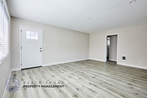 A spacious room with wooden flooring and two doors, one of which is open.