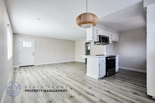 A spacious kitchen and living room with a wooden floor and white walls.