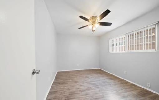 A room with a ceiling fan and a window with bars.