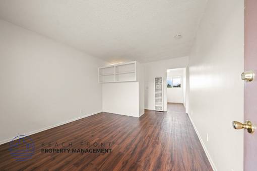 A room with wooden floors and white walls, with a door on the right side.
