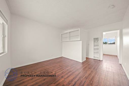 A room with wooden floors and white walls, with a window on the left and a door on the right.