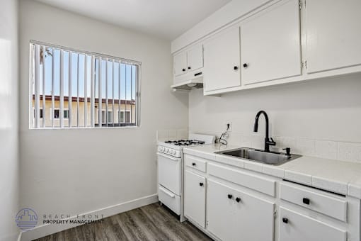 A kitchen with white cabinets and a window with blinds.