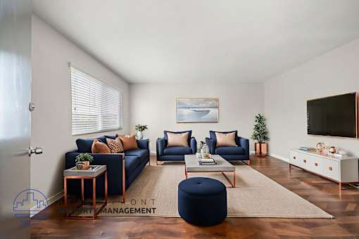 A living room with a blue ottoman and a television on the wall.