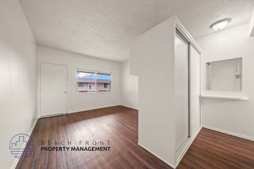A room with wooden floors and white walls, with a window showing a view of a building outside.