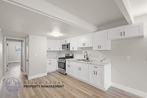 A kitchen with white cabinets and a logo for Beach Front Property Management.