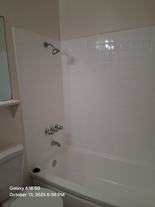 A white tiled bathroom with a shower and a toilet.