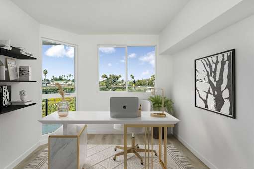 A room with a desk, laptop, and a framed picture on the wall.