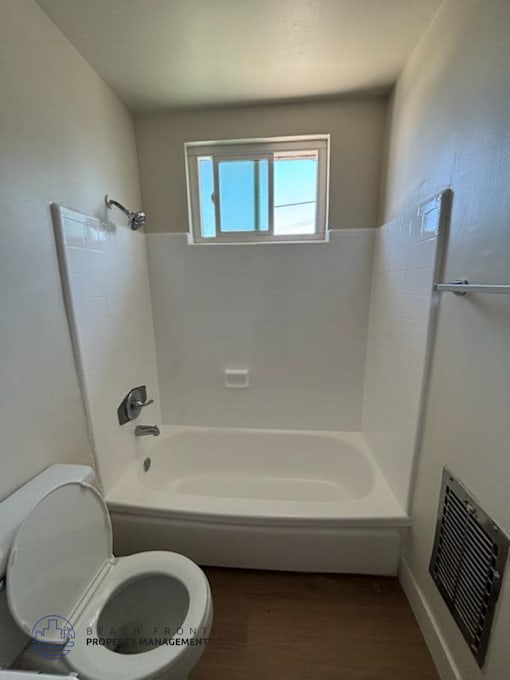 A white bathroom with a toilet, tub, and window.