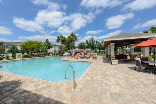 A swimming pool surrounded by a brick patio and lounge chairs.