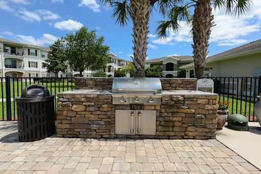 A stone fireplace with a grill on top is in the middle of a brick patio.