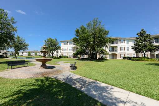 A park with a bench, a fountain and apartment buildings in the background.