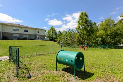 A green cylindrical object is in the foreground of a grassy area with a building in the background.
