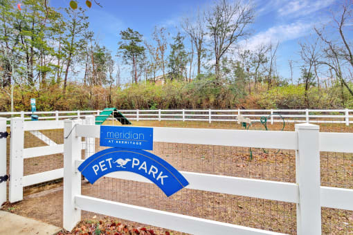 the entrance to the pet park with a white fence and a blue and white sign