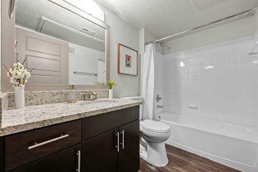 A white toilet sits in a bathroom with a marble countertop and a white bathtub.