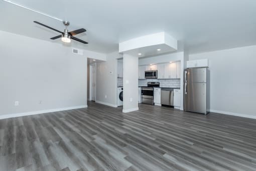 an empty living room with a kitchen and a ceiling fan