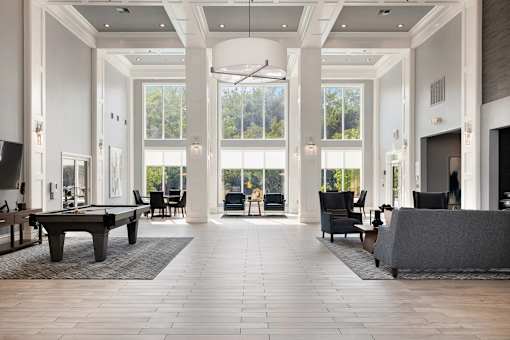 A large, open-concept living room with a pool table and a view of the trees outside the windows.