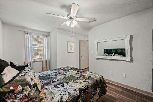 A bedroom with a floral bedspread and a white ceiling fan.