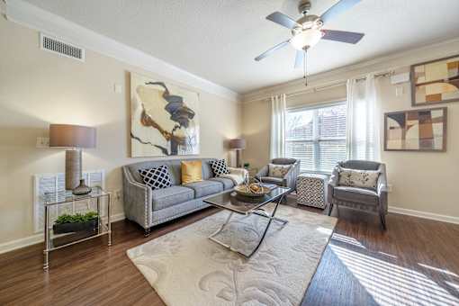 A living room with a grey couch, a glass table, and a ceiling fan.