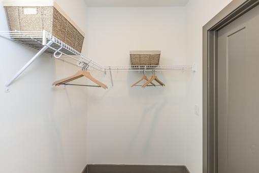 A white closet with a shelf and two hangers.