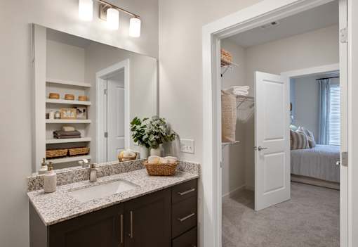 A bathroom with a large mirror above a sink with a basket of towels on the counter.
