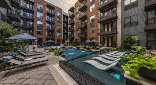 A pool surrounded by lounge chairs and umbrellas in a courtyard.