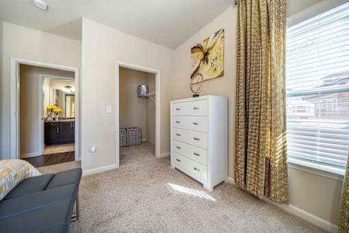 A room with a white dresser and a window with gold curtains.