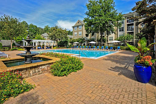 A pool surrounded by a brick patio and a fountain.