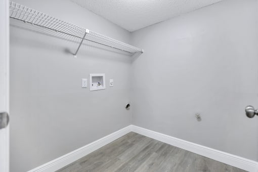 an empty room with white walls and wood flooring and a wire shelf on top