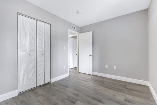 an empty room with white closet doors and a door to a hallway