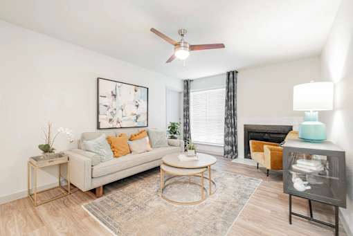 A living room with a grey couch, a coffee table, a side table, a fireplace, and a ceiling fan.