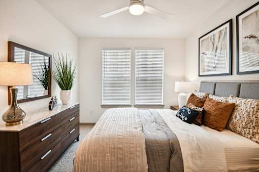 A bedroom with a bed, dresser, and window with blinds.
