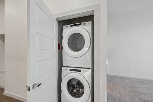 A white door is open to reveal a white washing machine and dryer.