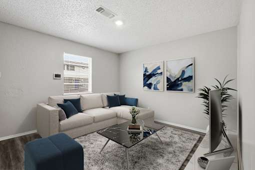 A living room with a white couch, a blue ottoman, a glass coffee table, and two abstract paintings on the wall.